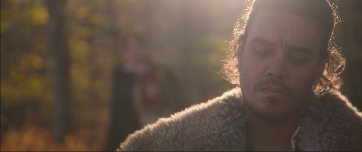Cynewulf in a sheepskin cloak, backlit in an autumn forest